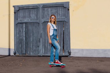 Tulum ve eski ahşap duvar yanında onun kaykay ile ayakta güneş gözlüğü giymiş bir gülümseyen kadın portresi.