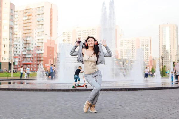 Girl listening to music streaming with headphones and dancing on the street.