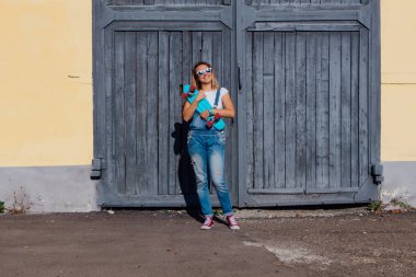 Eski ahşap duvar yanında onun kaykay ile ayakta bir gülümseyen kadın portresi.