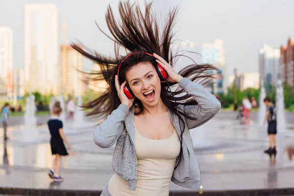 Girl listening to music streaming with headphones and dancing on the street.