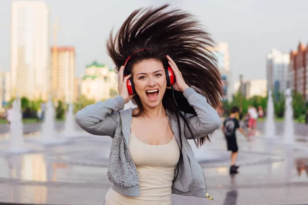 Girl listening to music streaming with headphones and dancing on the street.