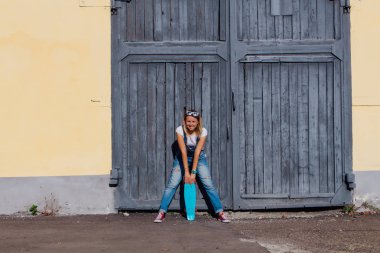 Tulum ve eski ahşap duvar yanında onun kaykay ile ayakta güneş gözlüğü giymiş bir gülümseyen kadın portresi.