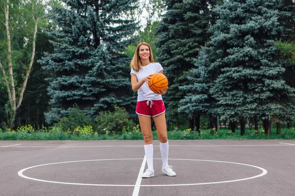 身穿白色T恤衫 短裤和运动鞋的漂亮金发姑娘在户外篮球场打球 复制空间 — 图库照片