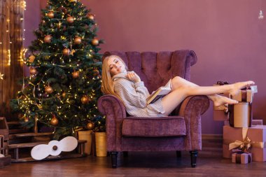 Güzel genç kadın rahat koltuk hediyeler ile Noel ağacı yanında oturan ve kitap okuma bir kazak giymiş. Noel rahat fotoğraf