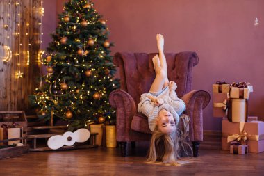 Güzel genç kadın ile hediyeler Noel ağacının yanındaki tarafı yukarı rahat koltuk döşeme kazak giymiş. Noel rahat fotoğraf
