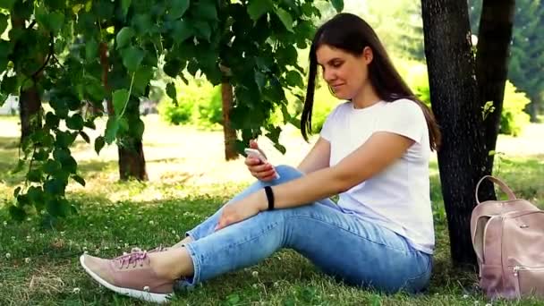 Jonge vrouw zittend op het gras met een mobiele telefoon — Stockvideo