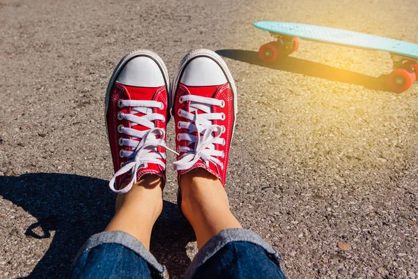 Close up of feet of a girl in red sneakers and blue plastic penny skate board with pink wheels on the background. Urban scene, city life. Sport, fitness lifestyle.