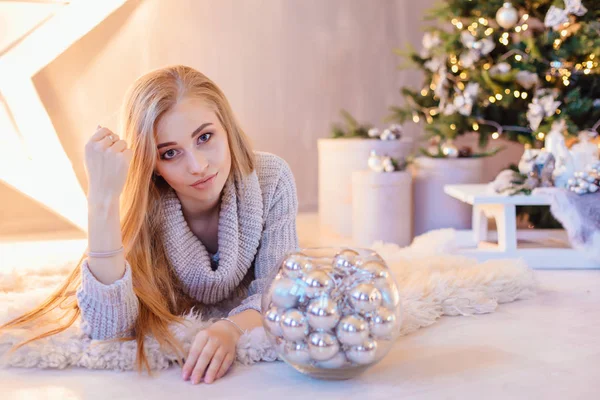 ボウル休日インテリアにはシルバー ボールの完全なクリスマス ツリーとの大スターの横に敷設白いセーターに身を包んだ若いブロンド美人 — ストック写真