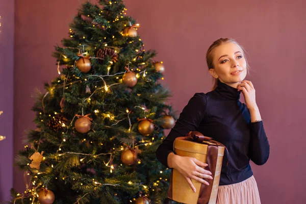 Noel ağacının yanındaki uzun sarı holding mevcut kutusuyla güzel genç kadın. Noel glamour fotoğraf