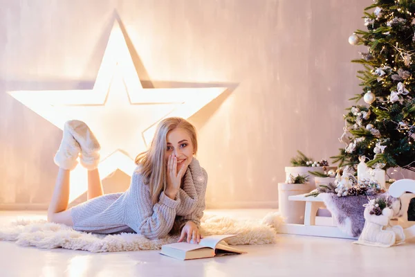 La mujer hermosa joven que pone y que lee el libro bajo el árbol de Navidad en el interior de fiesta —  Fotos de Stock