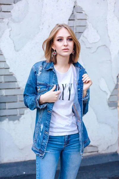 Fashion girl standing near brick wall in denim oversized jacket and beautiful ear rings.