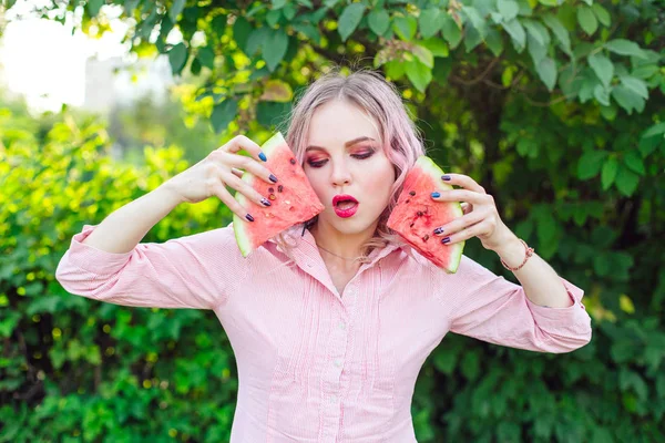 Mulher bonita com cabelo rosa segurando duas fatias de melancia na frente de seu rosto — Fotografia de Stock