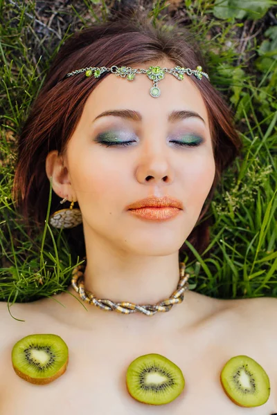 Красива молода азіатка лежить на траві зі скибочками ківі на грудях — стокове фото