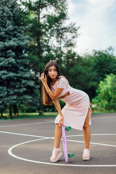 Portret van een lachende charmante brunette vrouw houdt haar skateboard op een basketbalveld. — Stockfoto