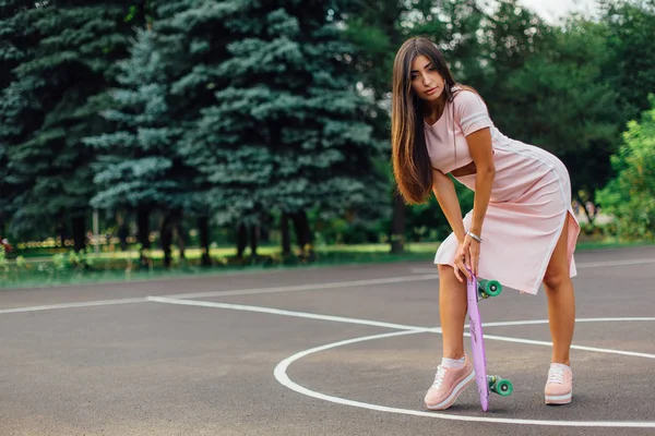 Portret van een lachende charmante brunette vrouw houdt haar skateboard op een basketbalveld. — Stockfoto