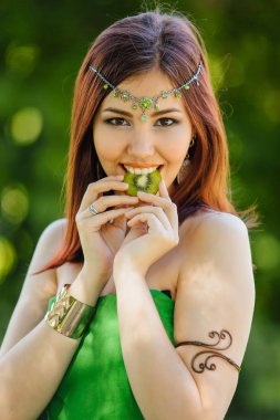 Yeşil elbise ve diadema dilim kivi ısırma kafasına güzel genç Asyalı kadın portresi