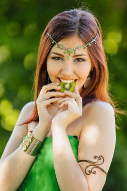 Yeşil elbise ve diadema dilim kivi ısırma kafasına güzel genç Asyalı kadın portresi