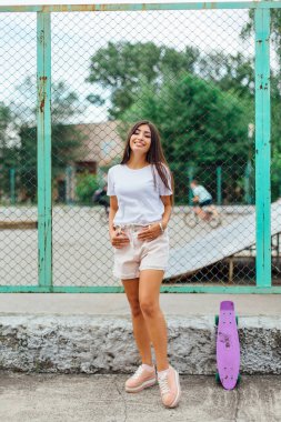 Yaz yaşam tarzı görüntü trendy genç ve güzel kız onun mor plastik scateboard ile scateboard coart yanında ayakta.