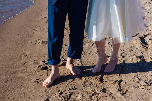 Front view of wedding couple\'s feet standing on the sandy beach.