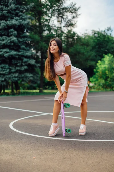 Potret seorang wanita berambut cokelat yang menawan sedang memegang skateboard di lapangan basket . — Stok Foto