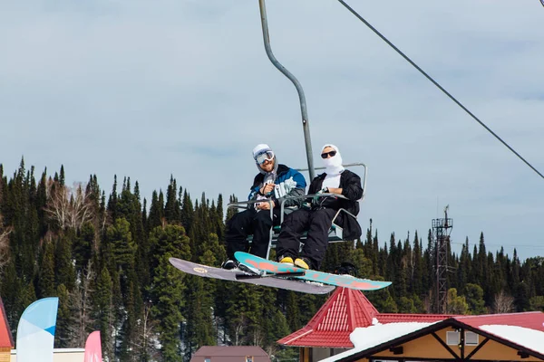 Sheregesh, Mountain Shoria, Kemerovo Region, Russia - April 6, 2018 : Couple of snowboarders on a ski lift in ski resort — Stock Photo, Image