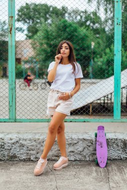 Yaz yaşam tarzı görüntü trendy genç ve güzel kız onun mor plastik scateboard ile scateboard coart yanında ayakta.