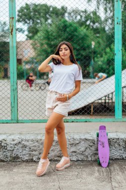 Yaz yaşam tarzı görüntü trendy genç ve güzel kız onun mor plastik scateboard ile scateboard coart yanında ayakta.