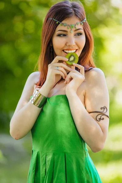Yeşil elbise ve diadema dilim kivi ısırma kafasına güzel genç Asyalı kadın portresi