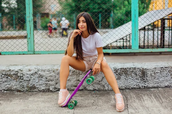 Mor plastik kaykayıyla kaykaylı coart 'ın yanında oturan trend bir genç kızın yaz yaşam tarzı görüntüsü.