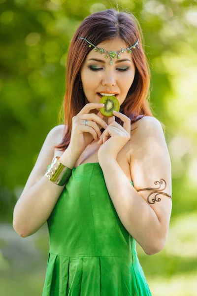 Yeşil elbise ve diadema dilim kivi ısırma kafasına güzel genç Asyalı kadın portresi