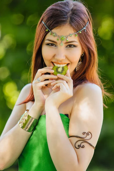 Yeşil elbise ve diadema dilim kivi ısırma kafasına güzel genç Asyalı kadın portresi