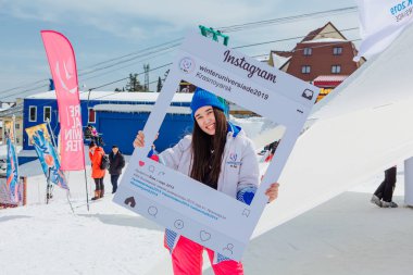 Sheregesh, Kemerovo bölgesi - 6 Nisan 2018. Genç kadın Dünya Üniversite Oyunları 2019 Instagram çerçeve tutan üniforma altında markalı. Krasnoyarsk Dünya Üniversite Oyunları 2019 bölgenin promo.