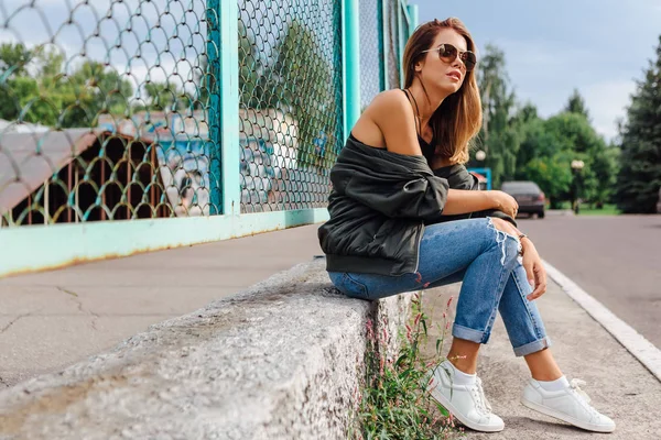 Moda portresi. Güneş gözlüğü takan genç bir kadın. Salonlu kot pantolon ve şehirde bombacı ceketi. Boşluğu kopyala.