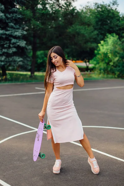 Portrait of a smiling charming brunette female holding her skateboard on a basketball court. — Stock Photo, Image