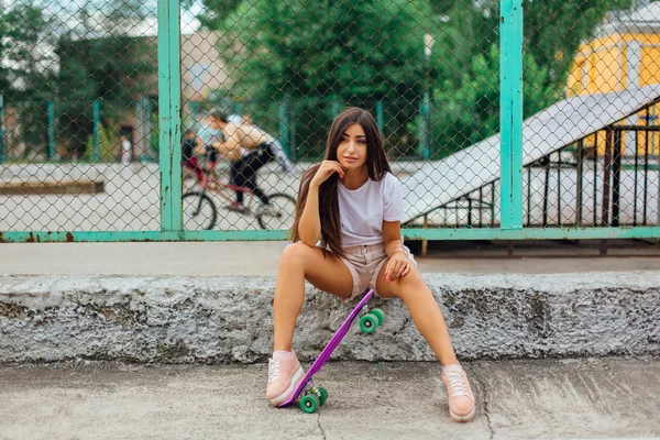 Verão estilo de vida imagem da moda muito jovem sentada ao lado do skate coart com seu skate de plástico . — Fotografia de Stock