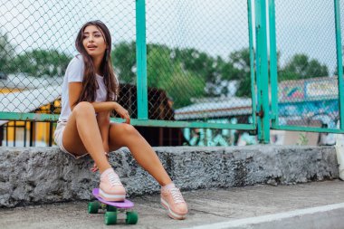 Yaz yaşam tarzı görüntü ile onun plastik kaykay kaykay coart yanında oturan trendy genç ve güzel kız.