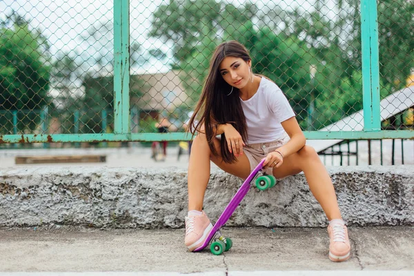 夏天生活方式的形象时尚漂亮的年轻女孩坐在滑板的旁边, 她的塑料滑板. — 图库照片