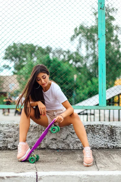 彼女のプラスチック スケート ボードとスケート ボード申し立てしている隣に座っているトレンディなプリティ少女の夏のライフ スタイル イメージ. — ストック写真