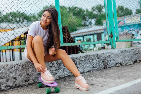 Зображення літнього способу життя модної красивої молодої дівчини, що сидить поруч зі скейтбордом зі своїм пластиковим скейтбордом . — стокове фото