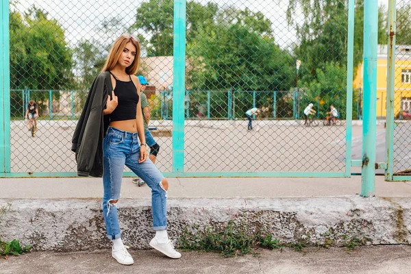 Retrato de moda de una joven de moda con gafas de sol, jeans con pasillos y chaqueta de bombardero en la ciudad — Foto de Stock