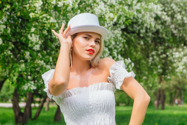 Sexy modern bride in white cylinder hat enjoing bloomin apple tree flowers. — Stock Photo, Image