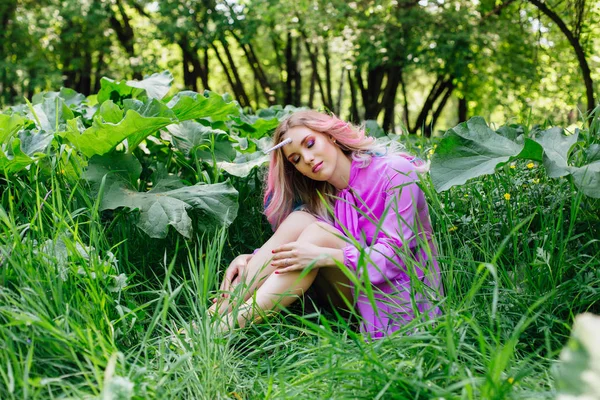 Chica de hadas unicornio con el pelo del arco iris y maquillaje brillante sentado en la hierba . — Foto de Stock