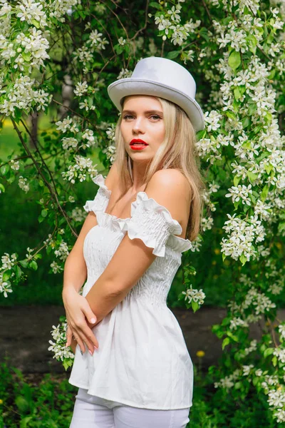 Sexy moderne bruid in witte cilinder hoed enjoing bloomin apple boom bloemen. — Stockfoto