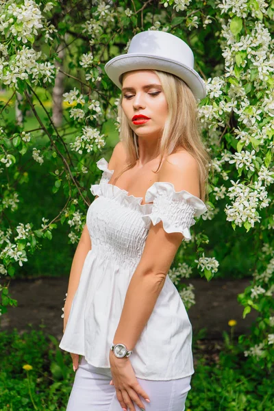 Sexy noiva moderna em chapéu de cilindro branco apreciando flores flor da árvore da maçã . — Fotografia de Stock