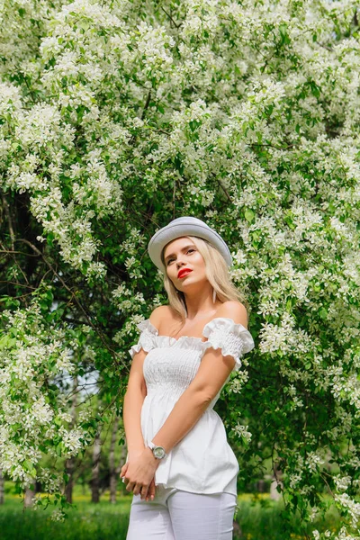 Szexi modern menyasszony fehér henger kalap fotózás, festészet virágzó apple tree virágok. — Stock Fotó