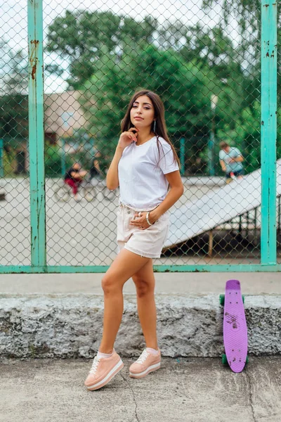 Estilo de vida de verano imagen de moda chica bastante joven de pie junto al coart scateboard con su scateboard de plástico . — Foto de Stock