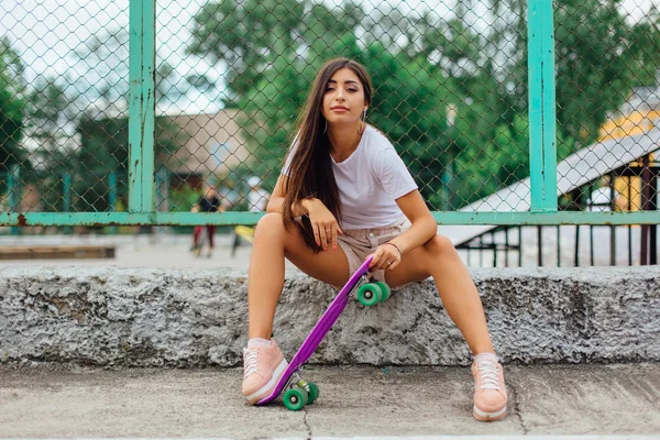 Verão estilo de vida imagem da moda muito jovem sentada ao lado do skate coart com seu skate de plástico . — Fotografia de Stock