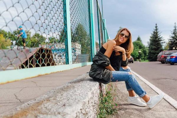 Retrato de moda de jovem na moda vestindo óculos de sol, jeans com salões e jaqueta de bombardeiro na cidade — Fotografia de Stock