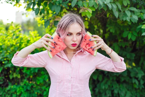 Mulher bonita com cabelo rosa segurando duas fatias de melancia na frente de seu rosto — Fotografia de Stock