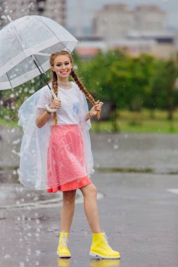 Genç güzel kız sarı çizmeli iki örgüler ve şeffaf şemsiye standları Çeşme yakınındaki.